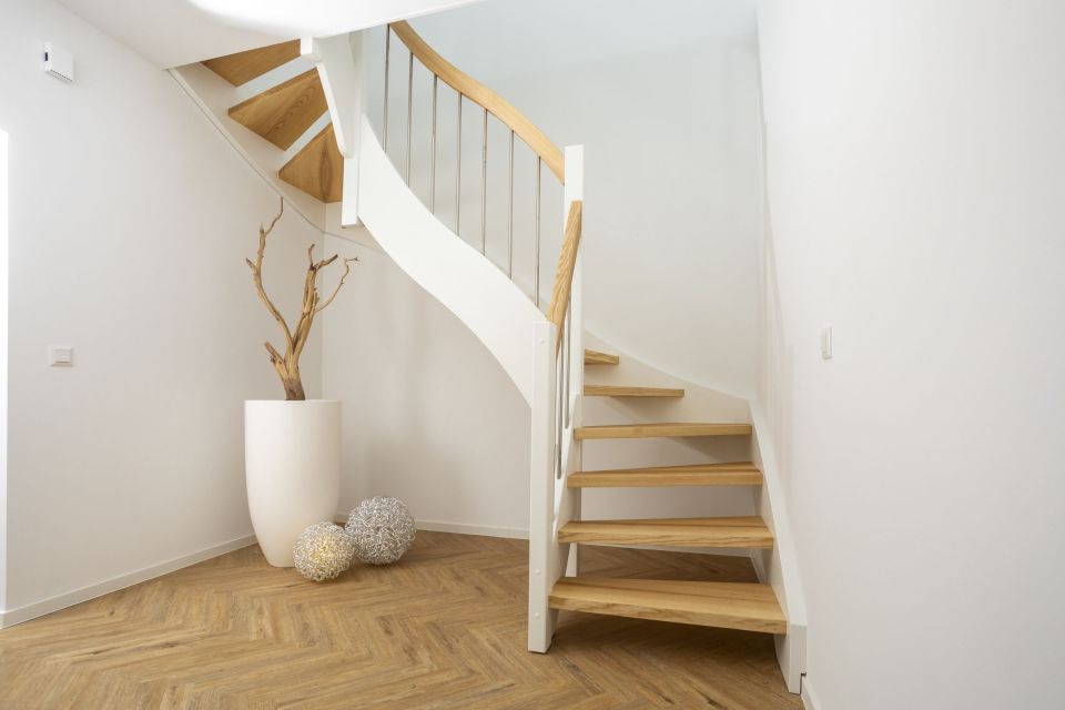 Moderner geschwungener Treppenaufgang mit Holzstufen, hellem Geländer und dekorativen Holzelementen.