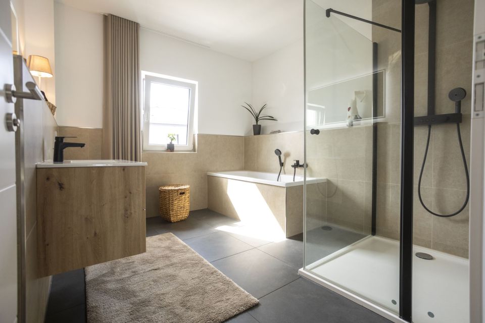 Modernes Badezimmer mit Badewanne, bodengleicher Glasdusche, Holzwaschtisch und schwarzen Armaturen.